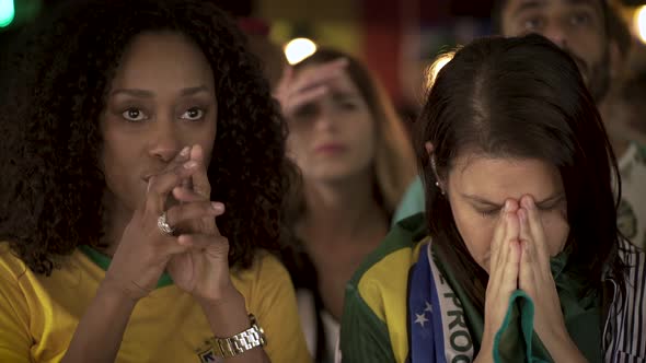 Brazilian football fans looking disappointed while watching televised match in bar alt