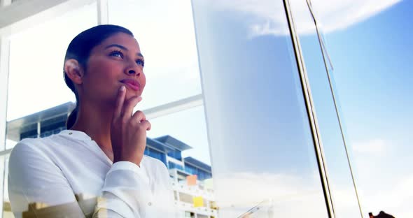 woman looking out office window and using smart device alt