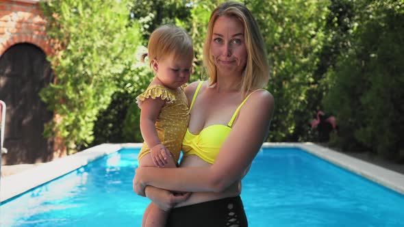 A nervous mother in a swimsuit holds a small crying child in her arms and calms him down alt