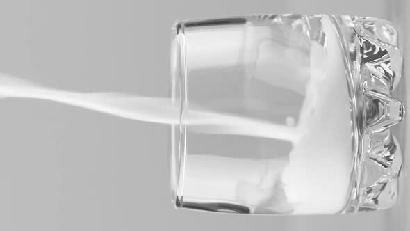 Vertical Video Milk Pouring Into Glass Close Up Isolated on Light Grey Background