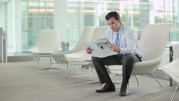Businessman reading a magazine then looking at the camera alt