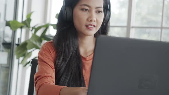 Beautiful Asian businesswoman wearing headphones using laptop conversation video call.