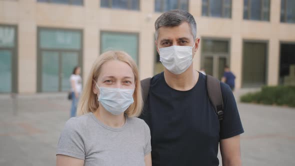 Portrait of Caucasian Young Man and Woman in Medical Masks Standing at Street and Looking at Camera