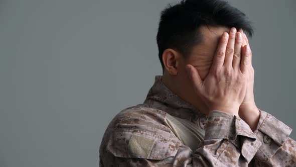 Upset military Asian man covering face with hands alt