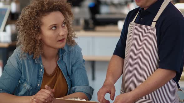 Caucasian waiter with down syndrome showing and discussing menu to the client at the cafe. Shot with alt