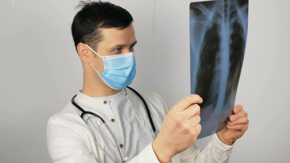 A Young Surgeon Wearing a Protective Medical Mask Examines an Xray of a Patient's Lungs and Ponders