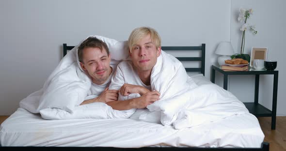 Young Gay Couple Lying on Bed Together in Bedroom Hugging and Kissing alt