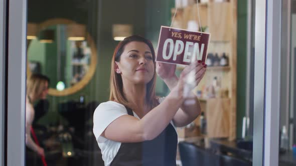 Female hairdresser changing sign board from Closed to Open at hair salon alt