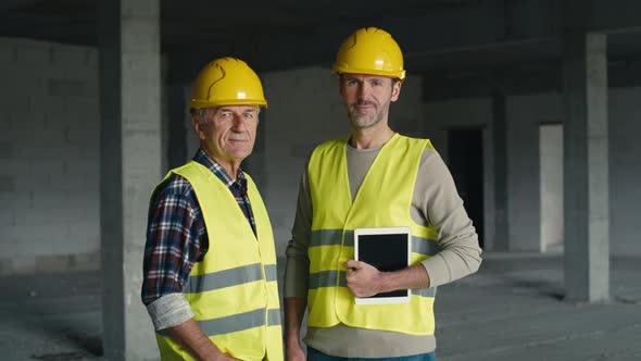 Portrait of two caucasian engineers holding digital tablet while standing on construction site. alt
