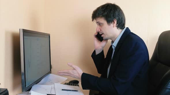 Frustrated Man Working at the Computer and Calling Mobile Phone