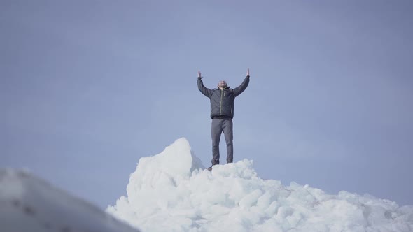 Emotional Happy Man in Warm Coat Standing on the Top of Glacier Throwing Up His Hands, Triumphing alt