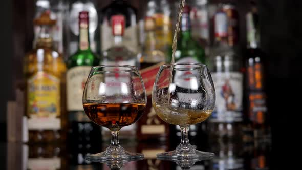 Closeup of a Bartender Slowly Pouring Cognac Into Two Glasses in a Bar alt
