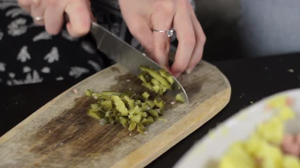Woman with sharp knife chop pickle into small cubes on wooden board alt