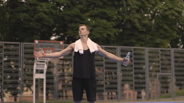Strong Young Man with Holding Hands Up While Standing on Outdoor Basketball Court alt