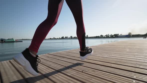 young athletic girl runs on pantone along the lake in black sneakers leggings alt