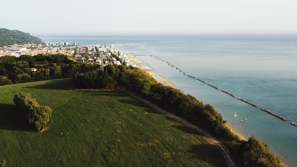 Drone Rising Above Green Tree Mountain Hill with Epic Sea View To Reveal Small Sunny Bay Town alt