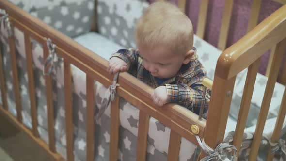 Little Baby Leans on Wooden Cot with Soft Linen at Home alt