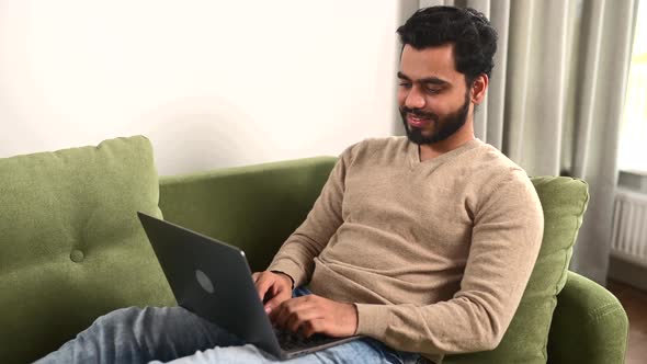 Optimistic Man Lying on the Couch and Using Laptop Computer for Messaging