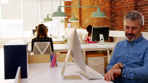 Male executive using smartwatch at desk alt