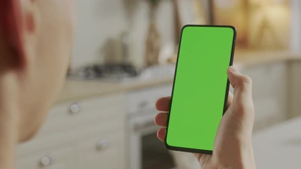Back View of Young Man at Home Sitting on Kitchen Room Using With Green Mockup Screen Smartphone alt