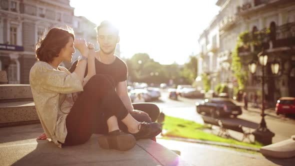 Young Beautiful Couple Taking Pictures Smiling Speaking Sitting in City Park alt