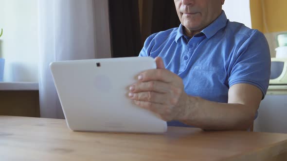 Aged Male Sits And Uses A White Tablet Pc At Home
