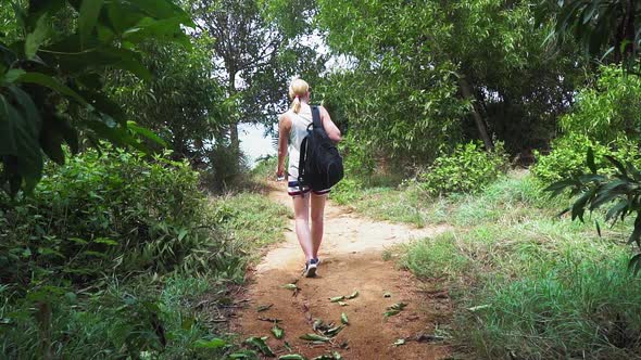 tourist girl with a backpack walking through the rainforest. comes out of the trees alt