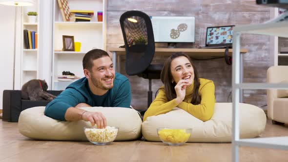 Cheerful Couple Watching Tv Sitting on Pillows alt