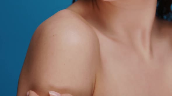 Close-up of Female Arm Moisturizing and Massaging Her Shoulder on Blue Background alt