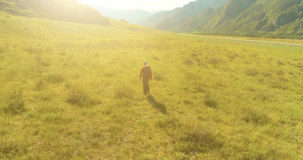 Flight Over Backpack Hiking Tourist Walking Across Green Mountain Field. Huge Rural Valley at Summer alt