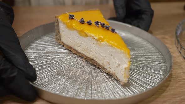 Female Hands Put Plate with Cheesecake with Jam on Table alt