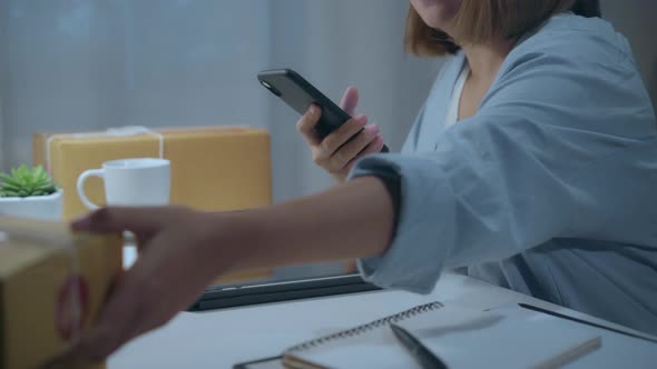 Asian young woman owner of SME online checking product on stock and save to mobile phone working.