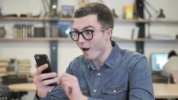 Excited Young Man Enjoying Success While Using Smartphone alt