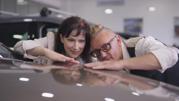 Portrait of Confident Successful Adult Couple Touching Luxurious New Car Hoods Talking in Slow alt