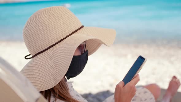 Coronavirus Vacation Woman in Face Mask Uses Phone App on Sea Beach in Summer