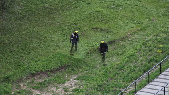 Two men mow grass with trimmers. 60 fps HD alt
