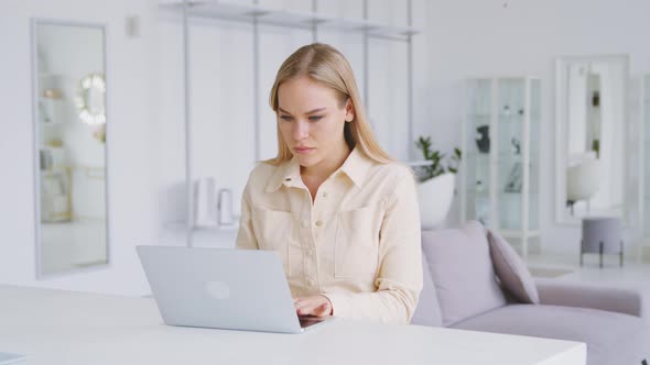 Thinking girl at the desk with a laptop in a white room. Portrait of young woman alt