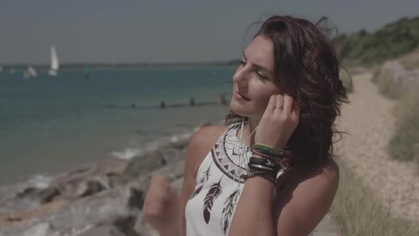 A Young Attract Woman Sat By The Sea Listening To Music On Head Phones - Ungraded alt