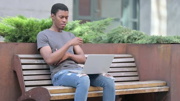 Young African Man Thinking and Using Laptop on Bench  alt