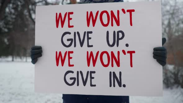 A Person is Standing in the Park Holding a Sign We Wont Give Up We Wont Give In. alt