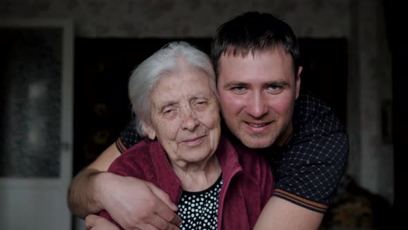 Grandson Son With A Smile Embraces Hugs His Old Elderly Grandmother Mother alt