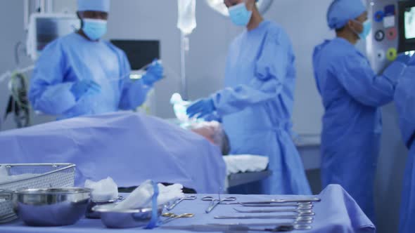 Mixed race surgeons wearing protective clothing putting patient to sleep in operating theatre alt