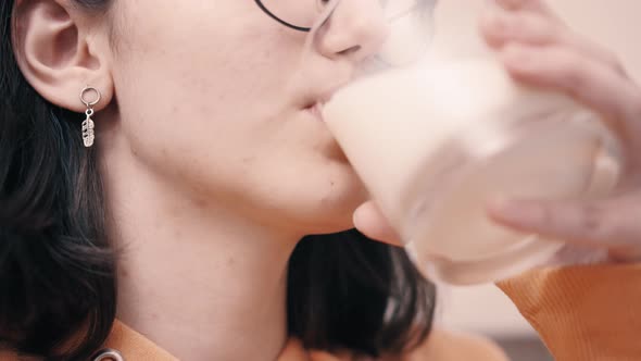 Unhappy Brunette Teen Girl Drinking Milk From a Glass and Smiling Closeup