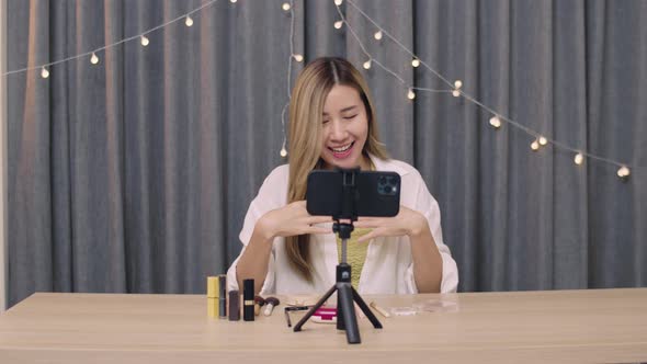 Asian female beauty blogger influencer makeup artist recording on smartphone educational tutorial.