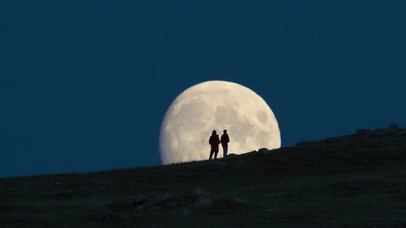 Silhouette of Woman and Child Standing Against Huge Moon Background.