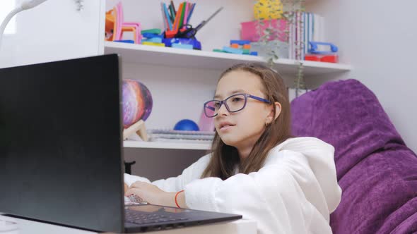 Portrait of a Girl Elementary School Student with Glasses Studying Remotely Online Using a Laptop