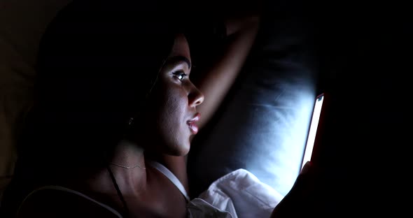 African American woman looking at phone while in bed at night.