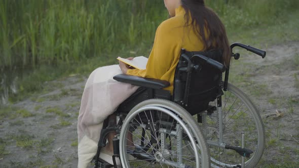 Back Angle View of Positive Disabled Young Woman Reading Book Outdoors. Confident Caucasian Lady on alt