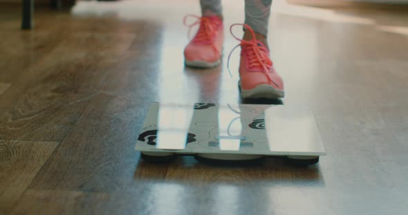 Weight Control Concept,women's Feet in Sports Shoes on the Floor Scales in the Living Room. alt