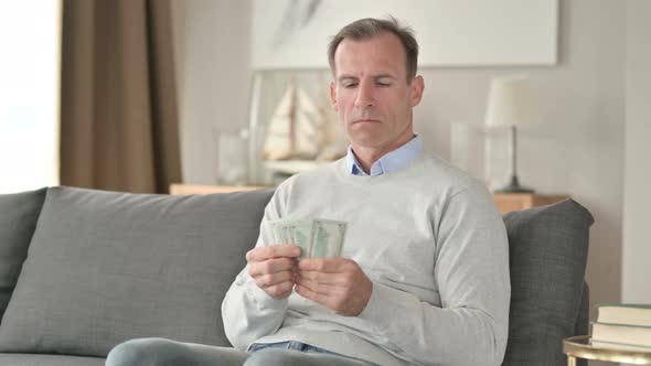 Serious Middle Aged Businessman Counting Dollar at Home  alt